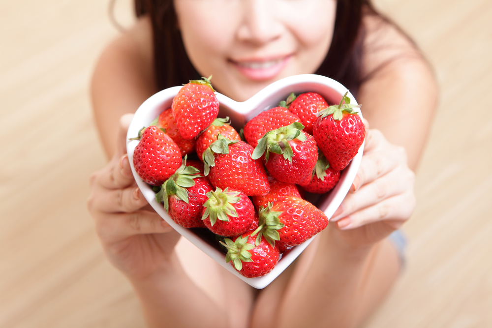 A woman holding a heartshaped bowl full of strawberries