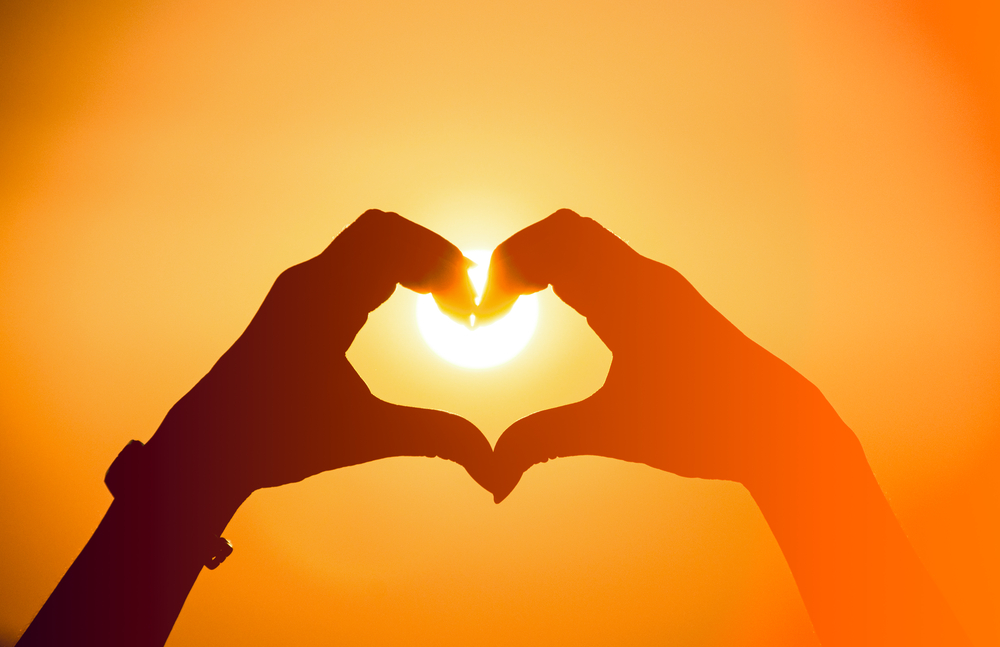 CLose up of two hands making a heart shape with the sun in the background