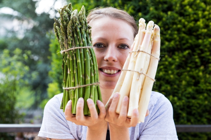 A woman holding a bunch of green asparagus and a bunch of white asparagus
