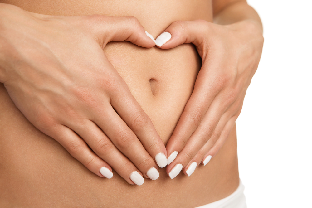 Close up on woman's stomach with hands making a heart shape to show a healthy tummy